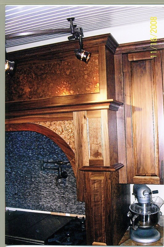Walnut range hood and mantel beneath a hammered-copper ceiling