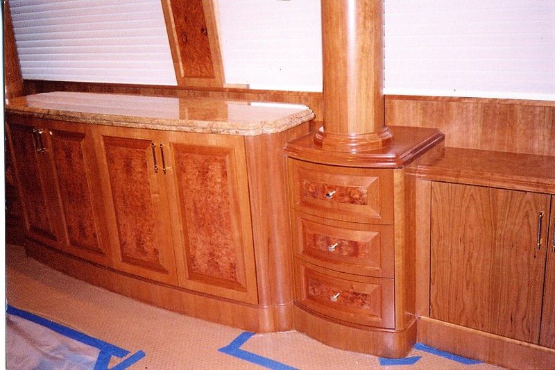 Curved yacht cabinetry with burl-wood panels, a turned column, and bow-front drawers