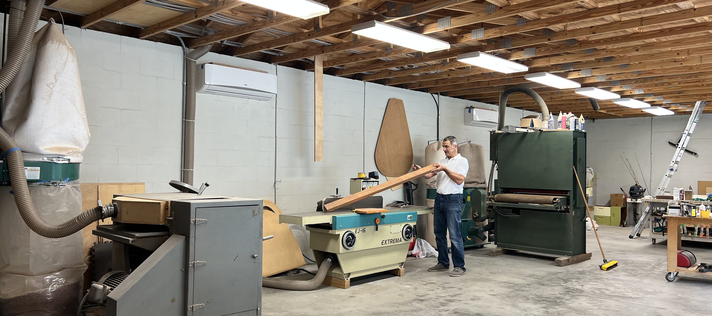 Jahija Ahmic at work in his Wesley Chapel shop, checking a board at the jointer, with the wide-belt sander and dust collection behind him